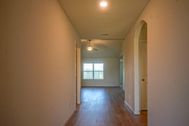 hall featuring wood finished floors, baseboards, and arched walkways