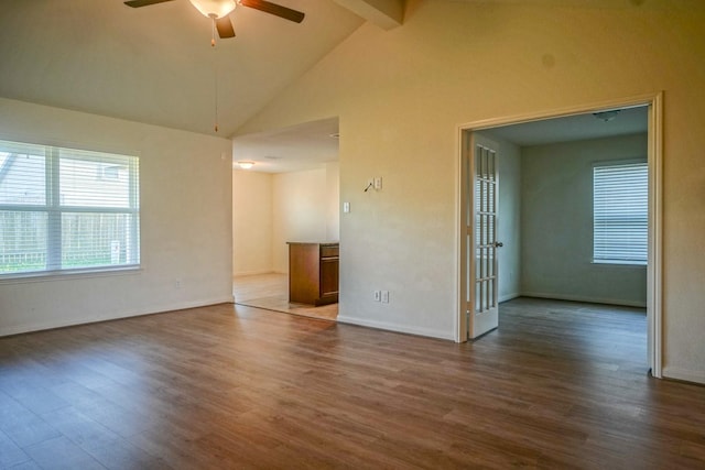 spare room with a ceiling fan, beamed ceiling, dark wood-type flooring, healthy amount of natural light, and baseboards