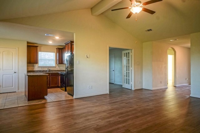 unfurnished living room with arched walkways, ceiling fan, beamed ceiling, wood finished floors, and high vaulted ceiling