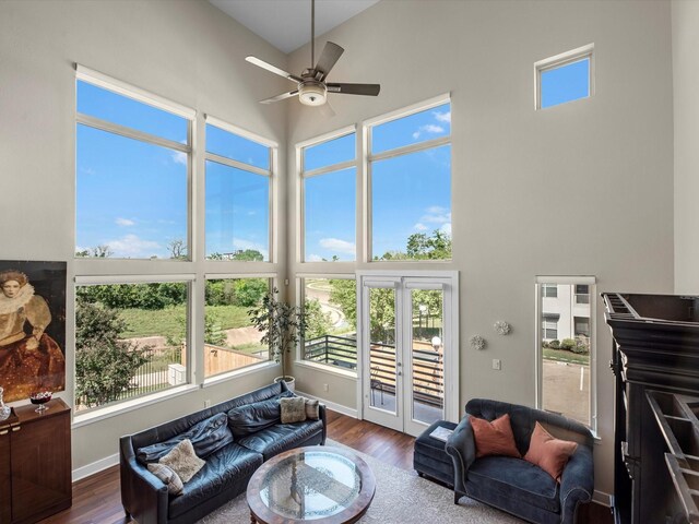 living area with wood finished floors, ceiling fan, baseboards, and a high ceiling