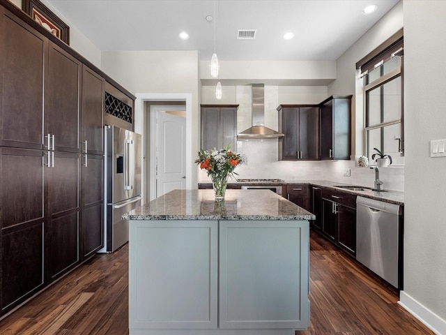 kitchen with stainless steel appliances, a sink, dark wood finished floors, wall chimney range hood, and light stone countertops