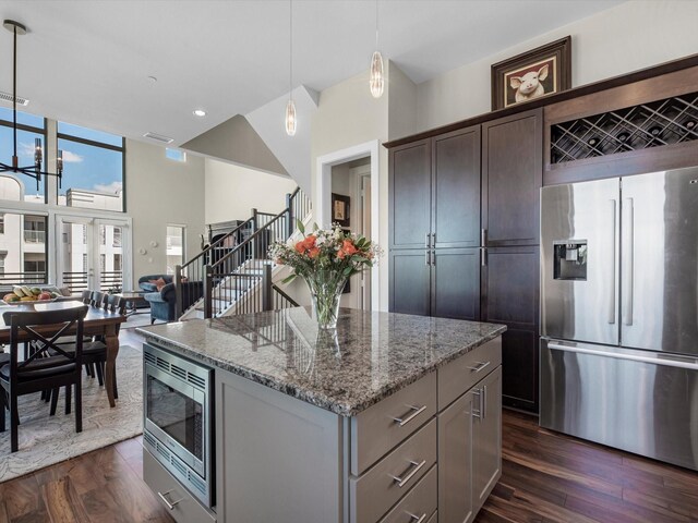 kitchen featuring dark wood-style floors, light stone counters, a kitchen island, pendant lighting, and appliances with stainless steel finishes