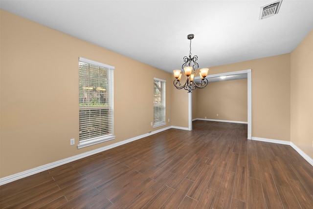 spare room featuring an inviting chandelier, dark wood-type flooring, visible vents, and baseboards