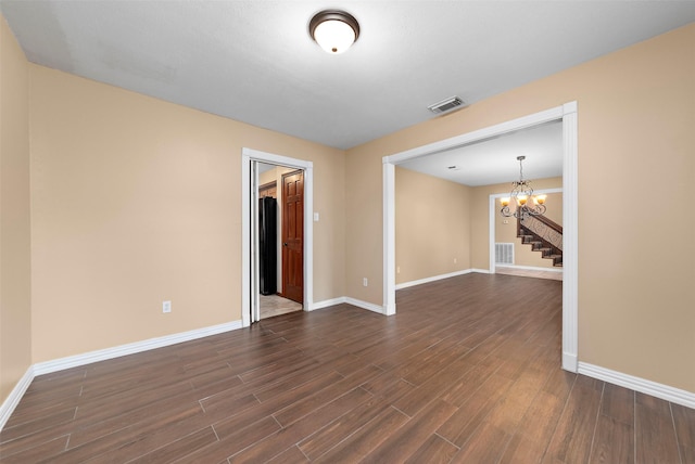 empty room featuring baseboards, visible vents, an inviting chandelier, and dark wood finished floors