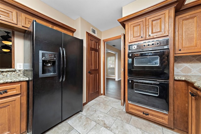 kitchen with brown cabinetry, visible vents, light stone counters, and black appliances