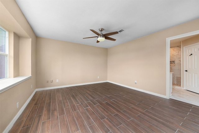 empty room with baseboards, visible vents, a ceiling fan, and dark wood-style floors