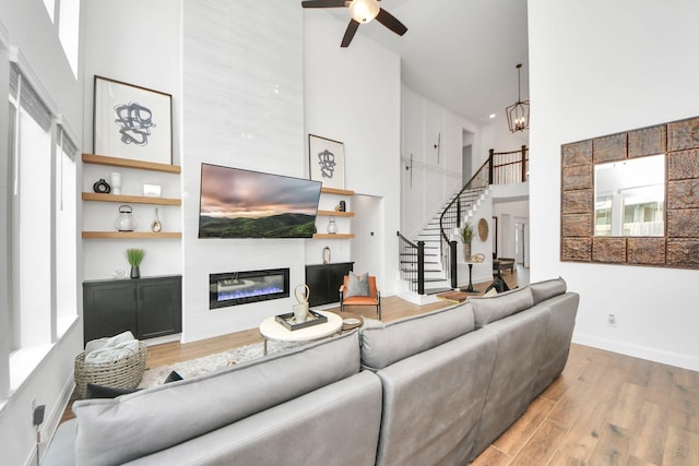 30706 Thicket Ct, Fulshear, TX 77441 - living room featuring a glass covered fireplace, ceiling fan with notable chandelier, wood finished floors, a high ceiling, and stairway