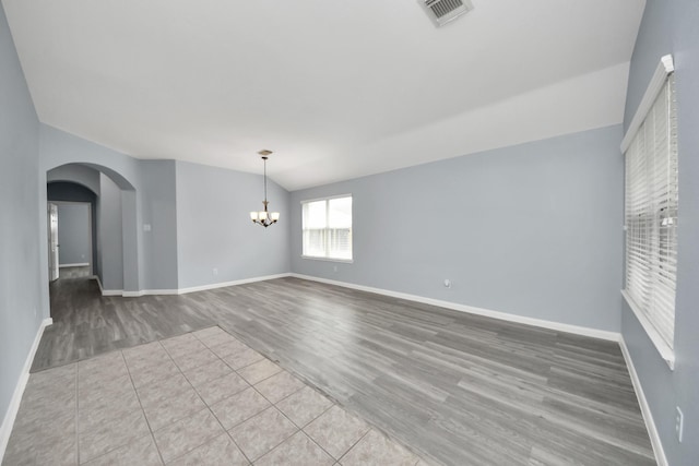 spare room featuring wood finished floors, visible vents, arched walkways, baseboards, and a chandelier