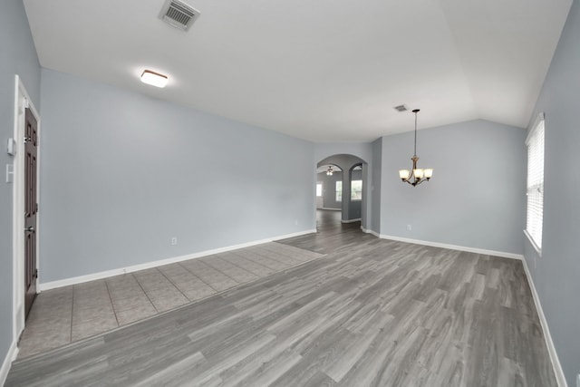 unfurnished room featuring lofted ceiling, wood finished floors, visible vents, arched walkways, and a chandelier