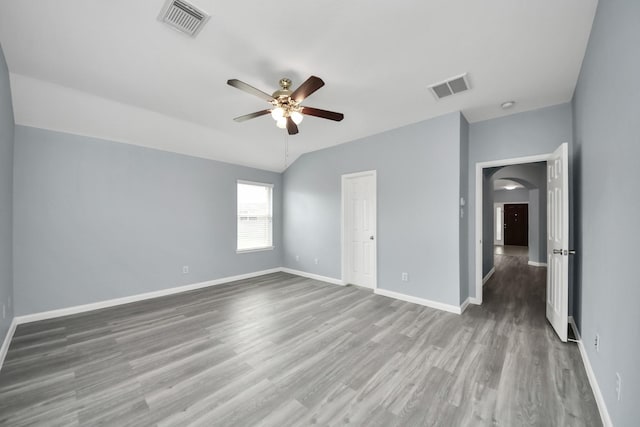 unfurnished bedroom featuring baseboards, wood finished floors, visible vents, and arched walkways
