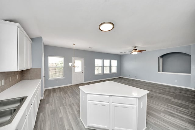 kitchen with white cabinets, a sink, tasteful backsplash, light wood-type flooring, and baseboards