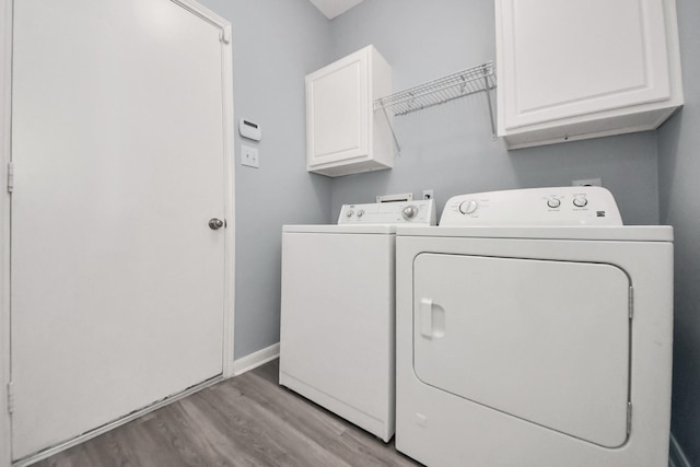 clothes washing area featuring washing machine and dryer, baseboards, cabinet space, and wood finished floors