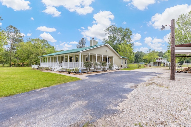 country-style home featuring aphalt driveway, a chimney, a porch, and a front lawn