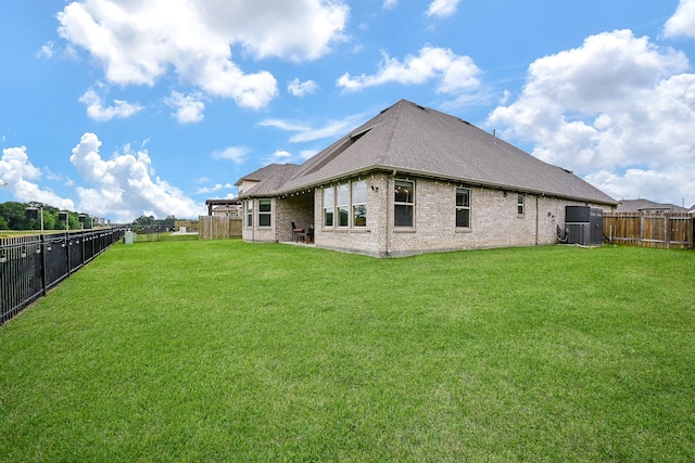 back of house featuring brick siding, a fenced backyard, a yard, and roof with shingles