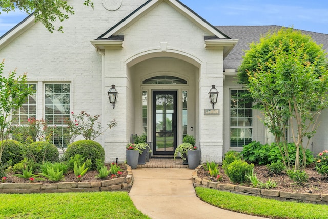 property entrance with a shingled roof and brick siding