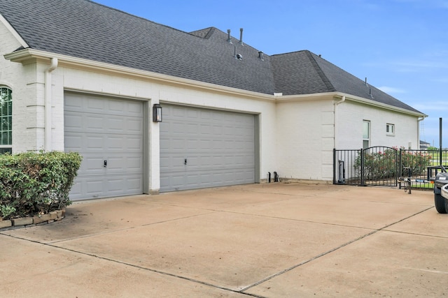 view of side of home with a garage, brick siding, a shingled roof, and concrete driveway