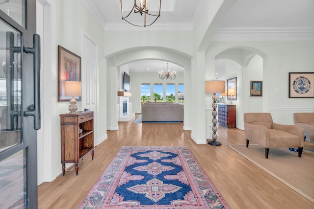 foyer with a chandelier, crown molding, baseboards, arched walkways, and wood finished floors
