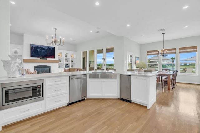 kitchen with appliances with stainless steel finishes, a chandelier, light wood finished floors, and a sink