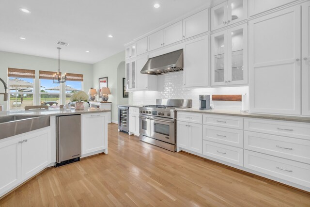 kitchen featuring wall chimney range hood, white cabinetry, a sink, range with two ovens, and wine cooler