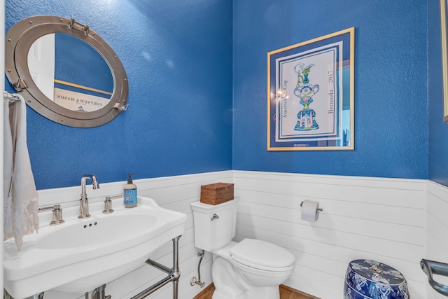 bathroom with a sink, toilet, a wainscoted wall, a textured wall, and wood finished floors