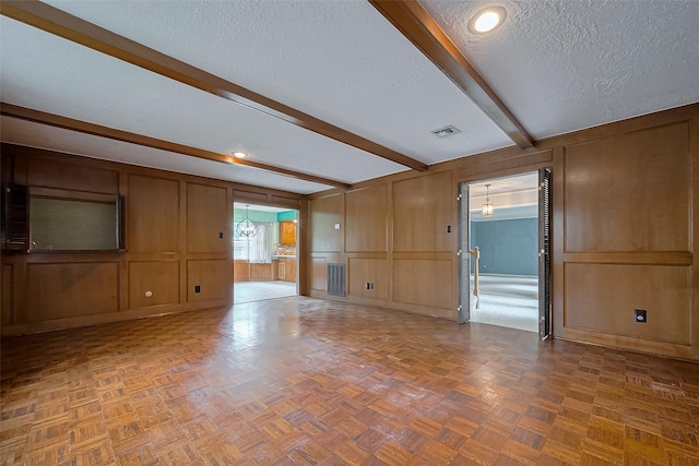 unfurnished room featuring a decorative wall, beamed ceiling, baseboards, visible vents, and a textured ceiling
