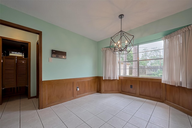 unfurnished dining area with an inviting chandelier, light tile patterned floors, and a wainscoted wall