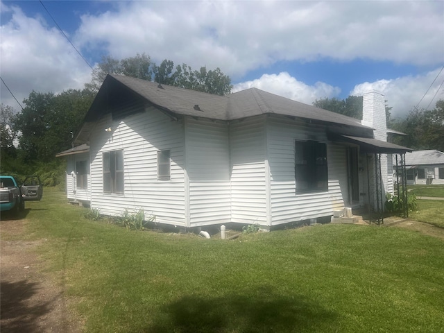 view of side of home with roof with shingles, a yard, and a chimney