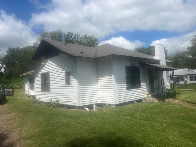 view of side of home featuring a chimney, a yard, and a shingled roof