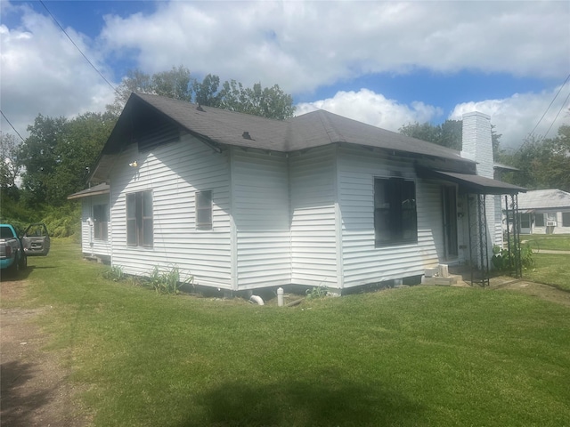 view of side of home with roof with shingles, a yard, and a chimney