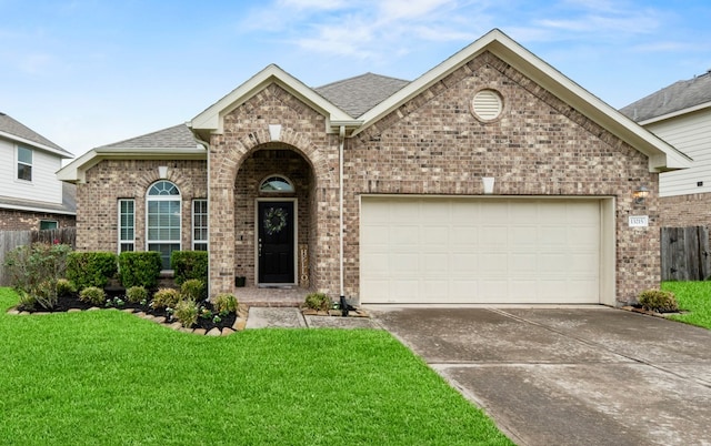 view of front of home featuring a shingled roof, an attached garage, brick siding, a front yard, and driveway