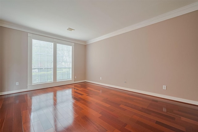 empty room with baseboards, visible vents, wood finished floors, and crown molding
