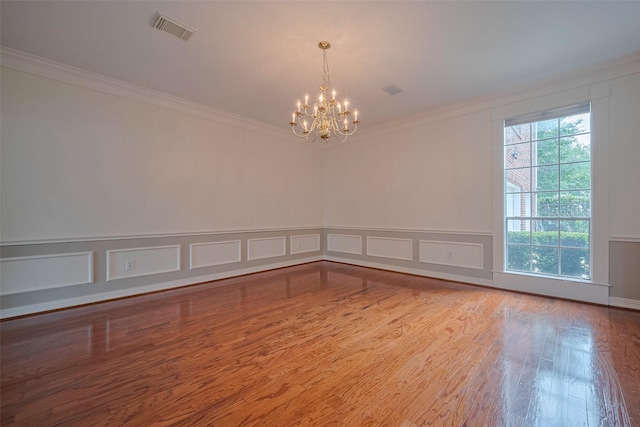 spare room featuring wood finished floors, a decorative wall, visible vents, a notable chandelier, and crown molding