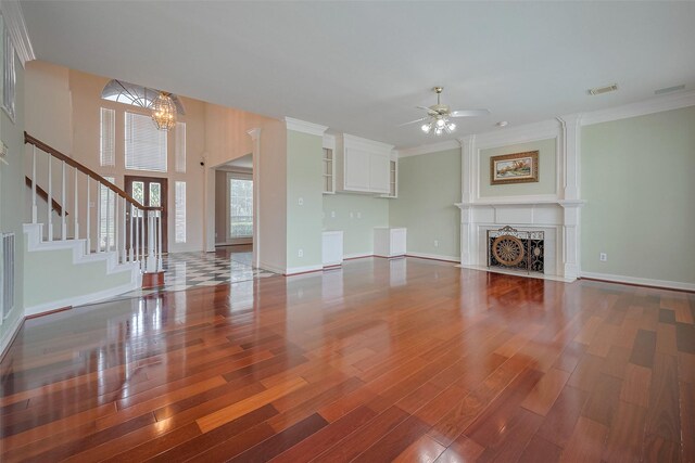 unfurnished living room with wood finished floors, ceiling fan with notable chandelier, baseboards, stairway, and a fireplace with flush hearth