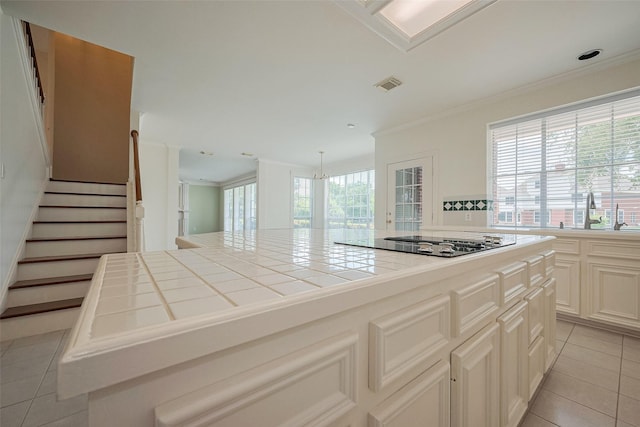 kitchen with black electric stovetop, a sink, light tile patterned flooring, ornamental molding, and tile countertops