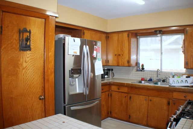 kitchen featuring backsplash, stainless steel refrigerator with ice dispenser, brown cabinets, a sink, and tile counters
