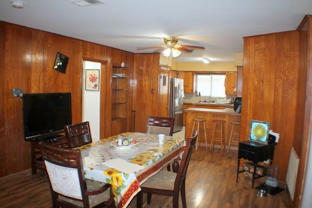 dining area featuring wood walls, a ceiling fan, dark wood-style flooring, and visible vents