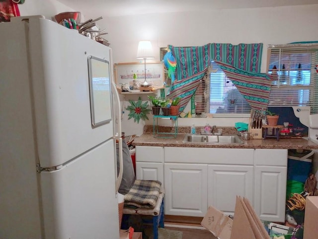 kitchen with freestanding refrigerator, a sink, and white cabinetry