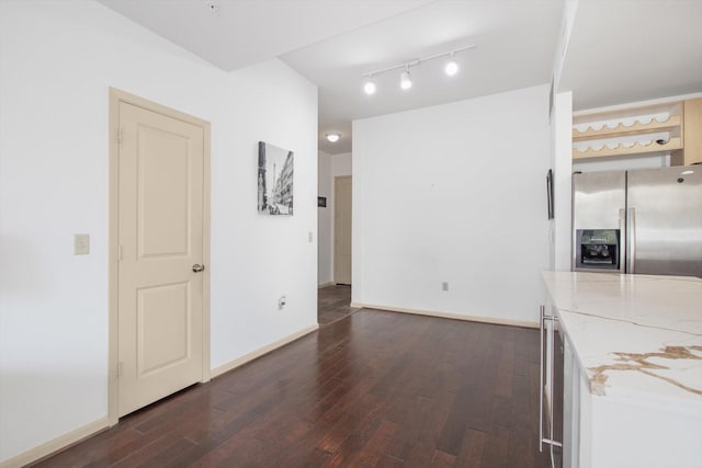 interior space featuring stainless steel refrigerator with ice dispenser, light stone countertops, dark wood-style floors, and baseboards