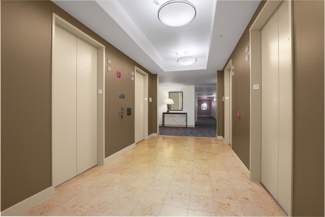 hallway with a raised ceiling, elevator, and baseboards
