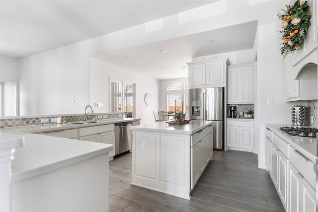 kitchen with decorative backsplash, a sink, appliances with stainless steel finishes, a center island, and dark wood-type flooring