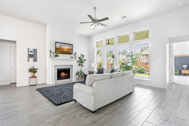 living area featuring a ceiling fan, visible vents, a lit fireplace, and light wood-style floors