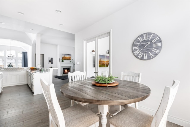 dining space with recessed lighting, arched walkways, a warm lit fireplace, light wood-style floors, and baseboards