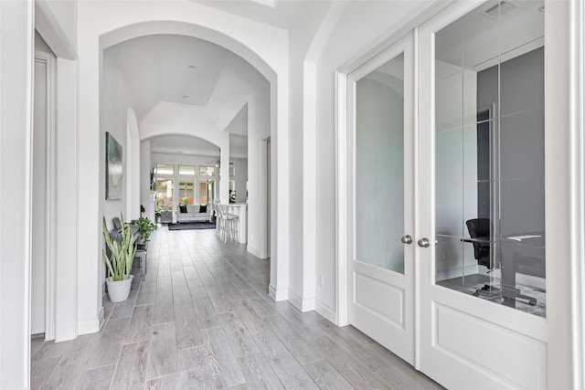 hall featuring visible vents, baseboards, arched walkways, light wood-type flooring, and french doors