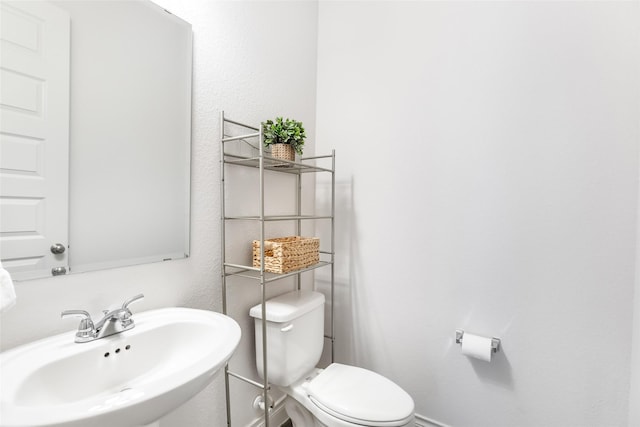 half bath with baseboards, toilet, and a sink