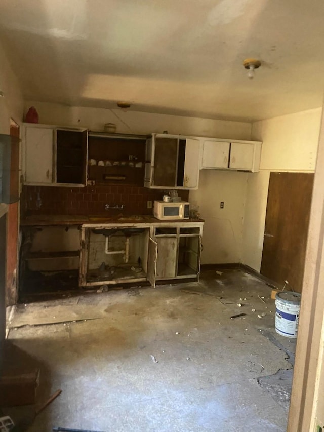 kitchen with white cabinetry, white microwave, and unfinished concrete floors