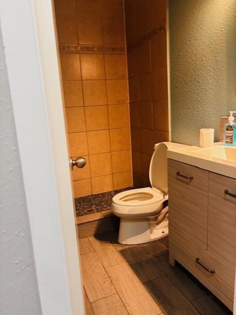 bathroom with toilet, vanity, a textured wall, and wood finished floors