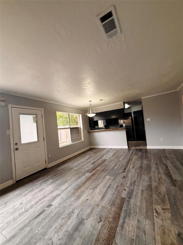 unfurnished living room featuring dark wood finished floors, visible vents, ornamental molding, and baseboards