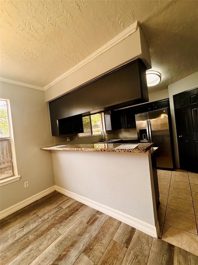 kitchen with a textured ceiling, crown molding, light wood-type flooring, stainless steel refrigerator with ice dispenser, and a peninsula