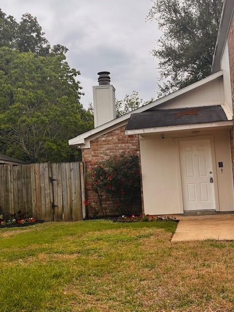 exterior space featuring a lawn, fence, a chimney, and brick siding