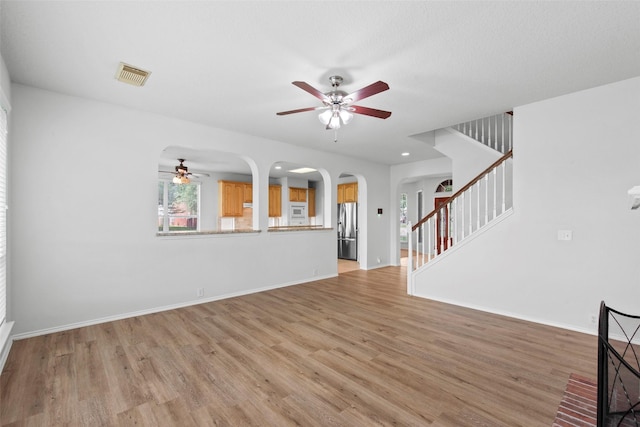 unfurnished living room featuring arched walkways, a wealth of natural light, light wood finished floors, visible vents, and a ceiling fan